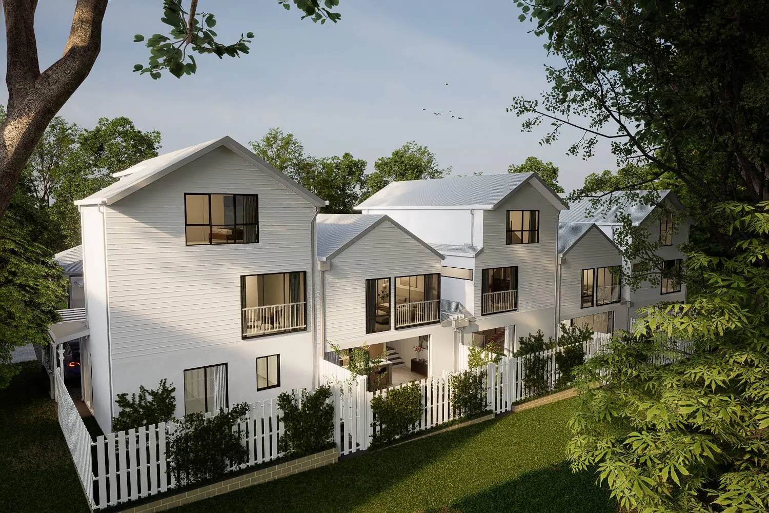 Elevated view along the row of white gabled townhouses, showing balconies, ground-floor living opening to the courtyards, and the mature trees of the reserve.